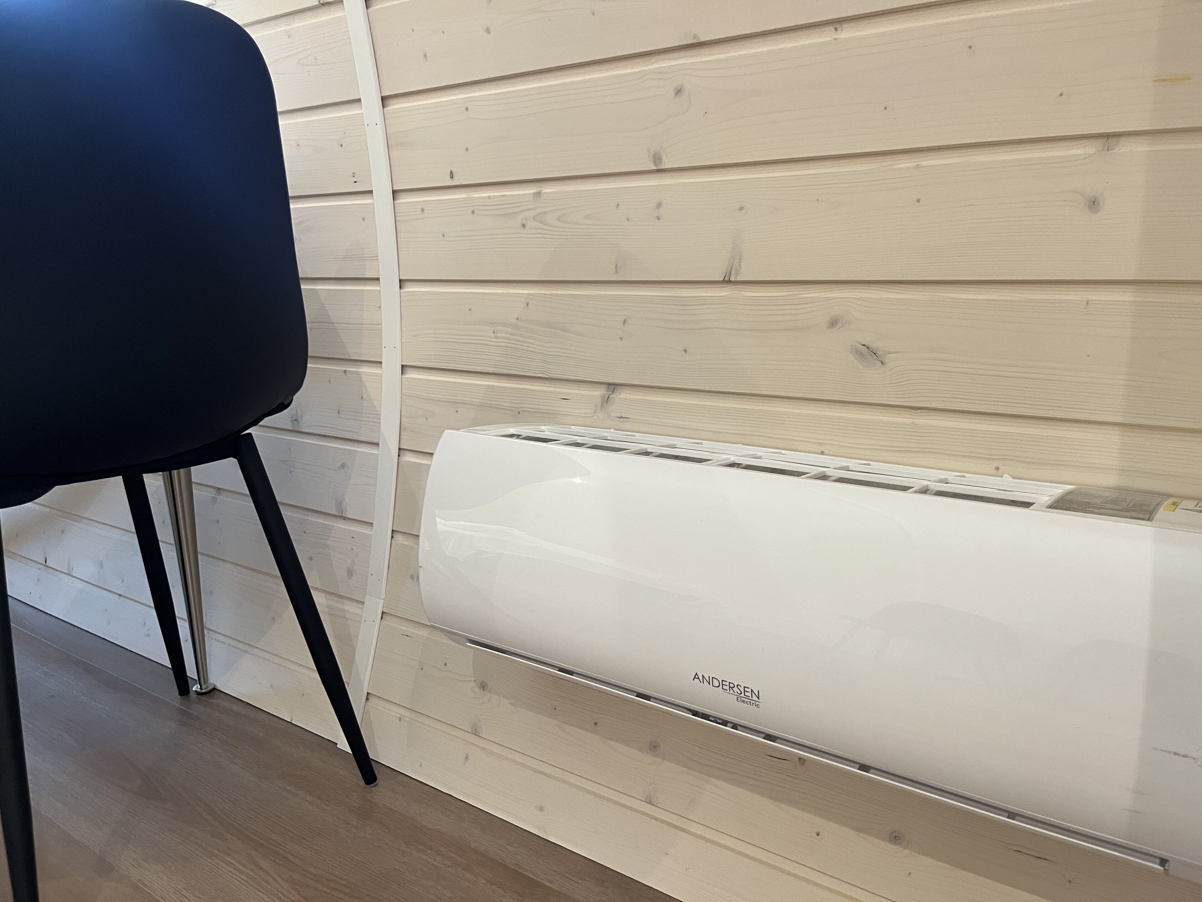 Un equipo de aire acondicionado blanco con la etiqueta 'ANDERSEN Electric' sobre un muro de madera.