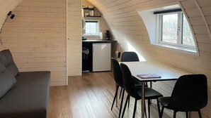 A cozy attic bedroom with a curved ceiling, a dining area with a table and chairs, and a kitchenette. - Helle Aktivitetshotel (Arre)