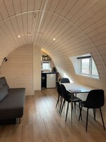 Um quarto de sótão acolhedor com teto curvo, sala de jantar com mesa e cadeiras, e uma cozinha compacta.
