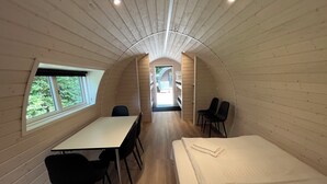A compact, cabin-style room with a long table and chairs, a bed, and a window with a view of greenery. - Helle Aktivitetshotel (Arre)