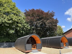 Two modern, semi-circular wooden cabins with built-in seating and a small table, set against a backdrop of trees and a clear sky. - Helle Aktivitetshotel (Arre)