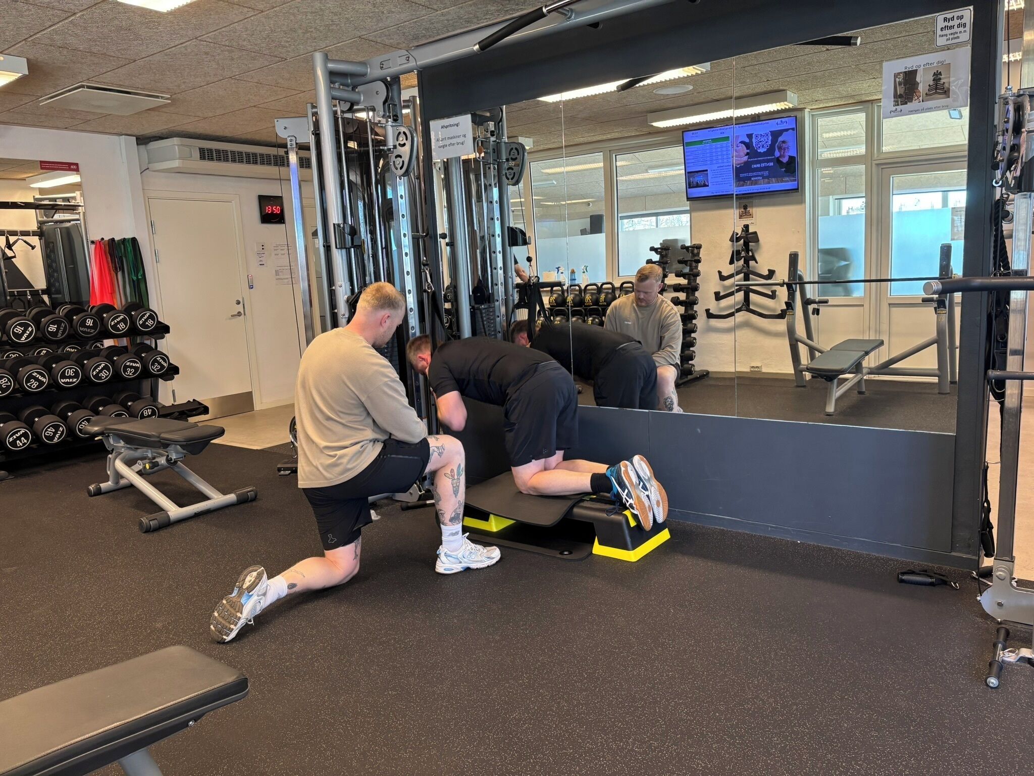 Ein Fitnessraum mit Gewichthebergeräten, einer Hantelbank und einem Spiegel, der den Raum wiederspiegelt.