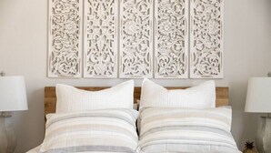 Een slaapkamer met een bed, twee kussens, een hoofdbord en een decoratief wandpaneel.