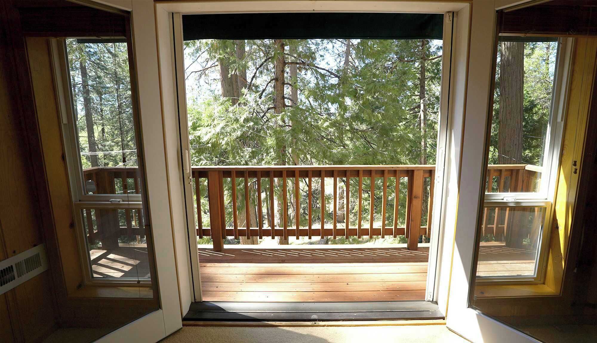 A wooden deck with a railing, leading to a forested area.
