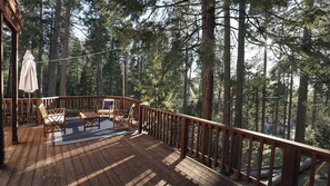 A wooden deck with outdoor furniture, surrounded by tall trees.