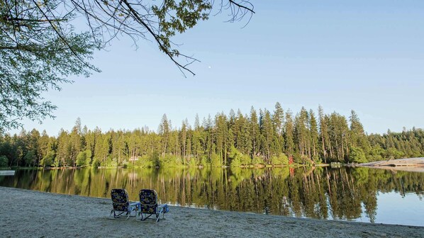 A serene lakeside view with two beach chairs and a clear reflection of trees.