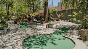 Un espace piscine avec un toboggan multicolore, entouré d’arbres et avec un bâtiment en arrière-plan.