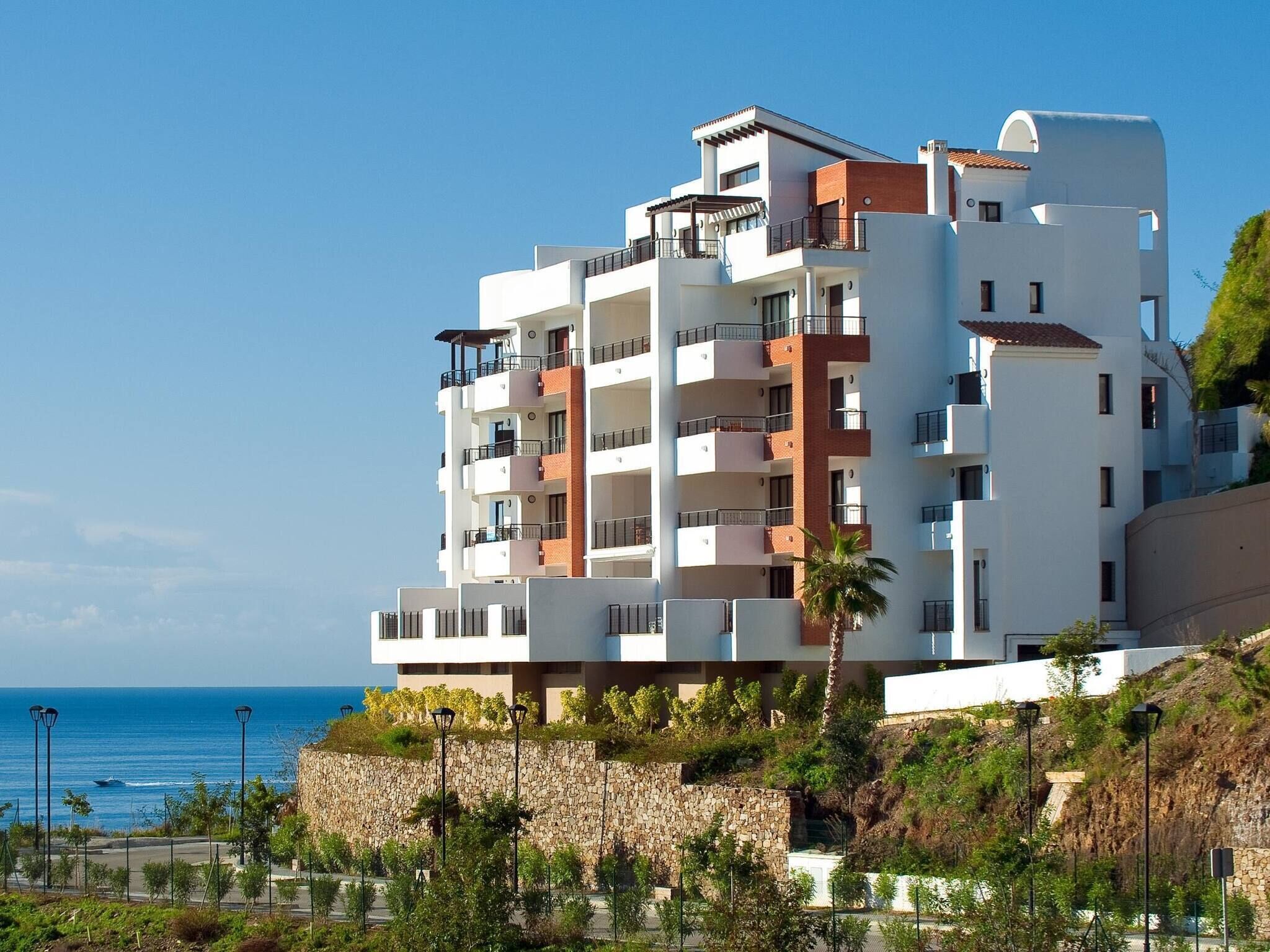 Un hotel a più piani con balconi, un muro di sostegno in pietra e vista sul mare.