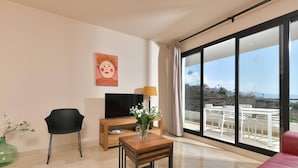 A modern living room with a sofa, a TV, a small table with a vase, and a view of a balcony with outdoor seating. - Apartamento con vistas al mar lateral (Torrox Costa)