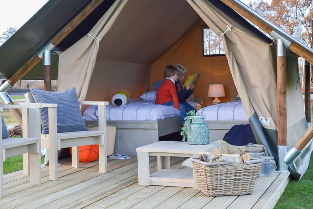 A cozy tented accommodation with two beds, a small table, and a wicker basket on the deck.