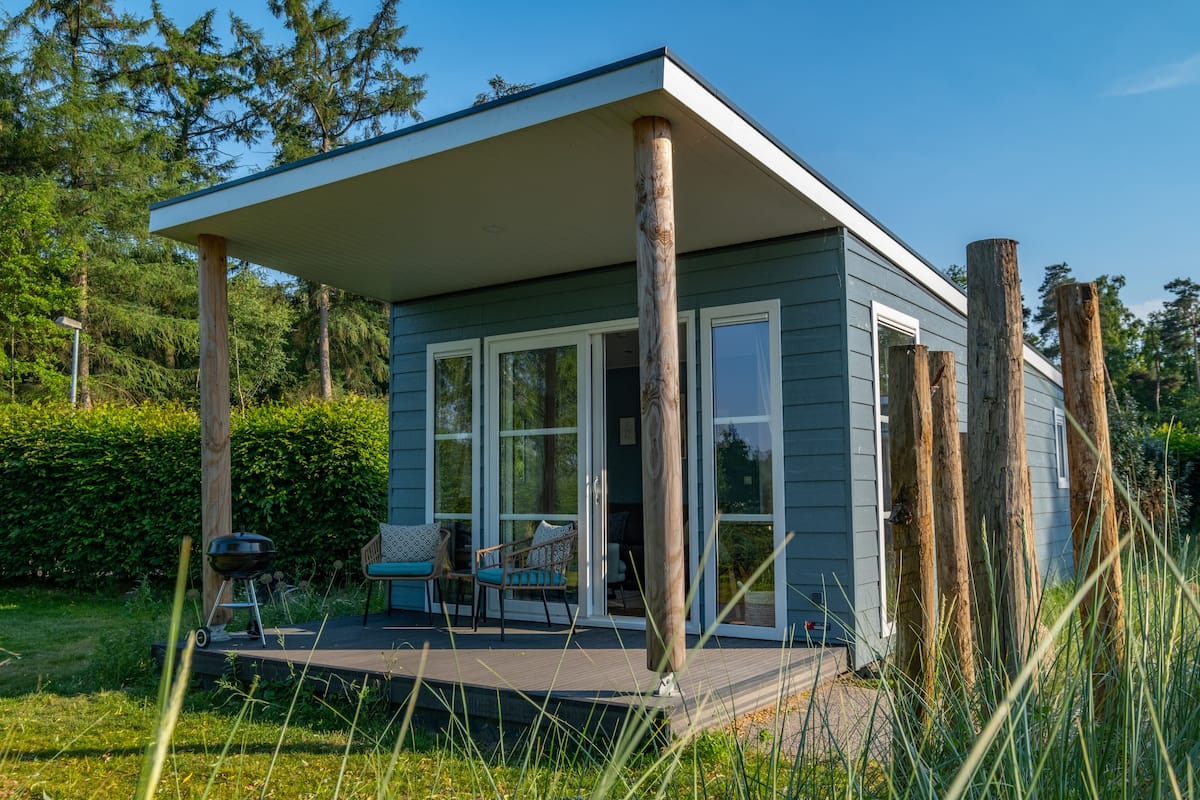 A modern house with a covered porch, large windows, and a barbecue grill.