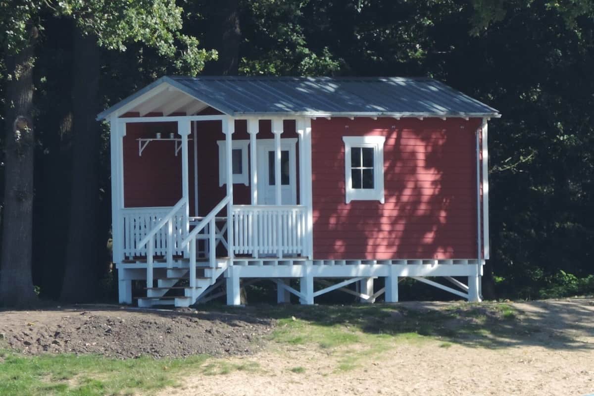A small, single-story cabin with a porch, surrounded by trees.