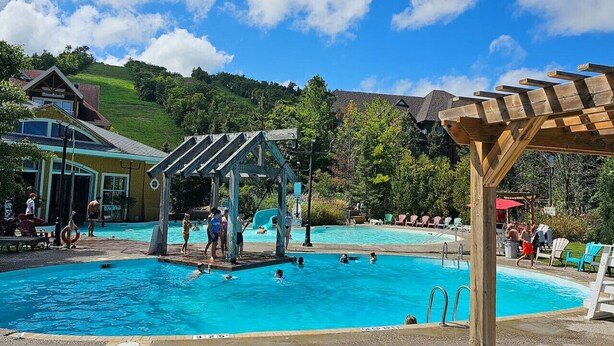 Un área de piscina con varias piscinas, una zona de estar cubierta y un edificio con techo inclinado.