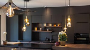 Een moderne keuken met donkere kastjes, hanglampen, een centraal eiland en een zithoek met tafel en stoelen.