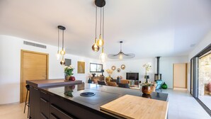 Een moderne keuken met een centraal eiland, hanglampen en uitzicht op de woonkamer.