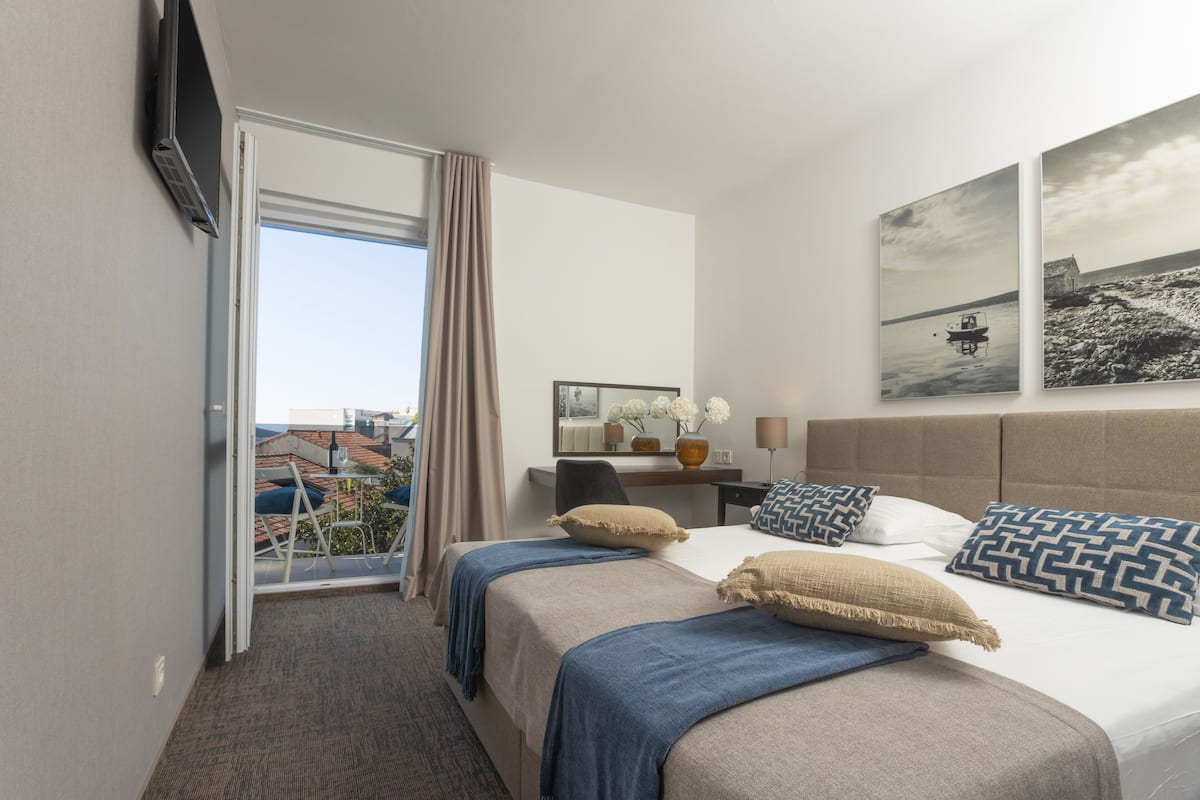 Ein Hotelzimmer mit Bett, Schreibtisch, Sessel, Fernseher und Fenster mit Blick auf Gebäude.