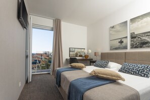 A hotel room with a bed, a desk, a chair, a TV, and a window with a view of buildings. - Villa Arausa (Vodice)