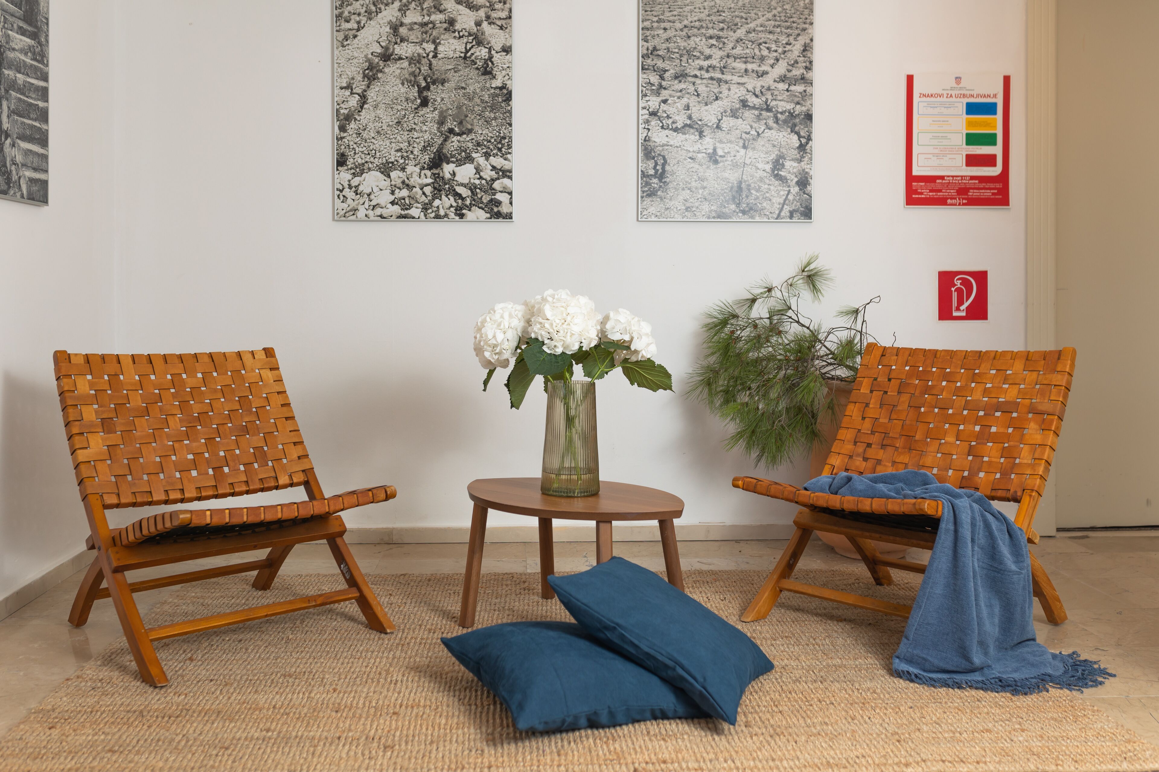 Dos sillones de mimbre, una mesita con un florero y un cojín azul sobre un suelo tejido.