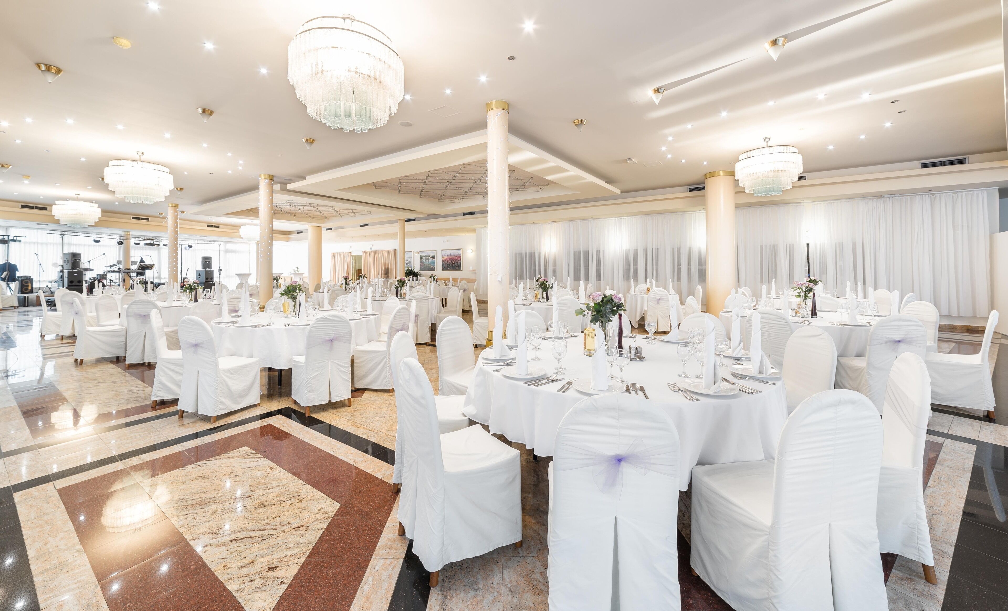 Un salón de banquetes con mesas redondas, sillas blancas, candelabros y un piso de mármol pulido.