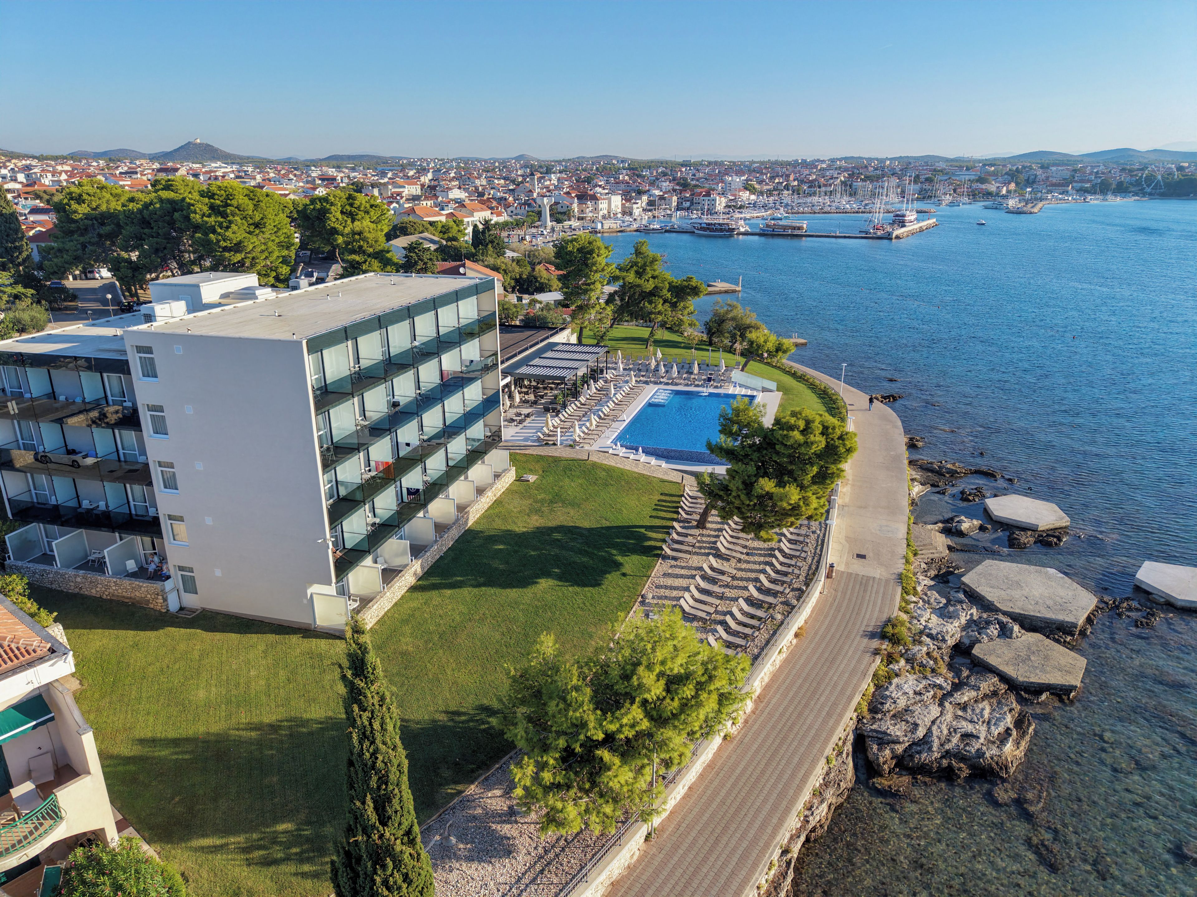 Un hotel costero con piscina, terraza y vistas al mar y al paisaje urbano.