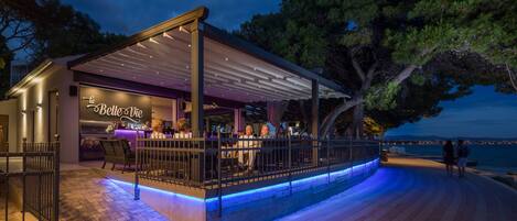 A waterfront bar with a covered seating area, outdoor lighting, and a view of the water.