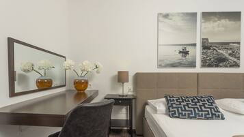A hotel room with a bed, a desk, a chair, a lamp, and two framed pictures on the wall.