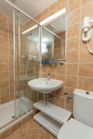 A bathroom with a glass shower enclosure, a white sink, a mirror, and a toilet. - Villa Arausa (Vodice)