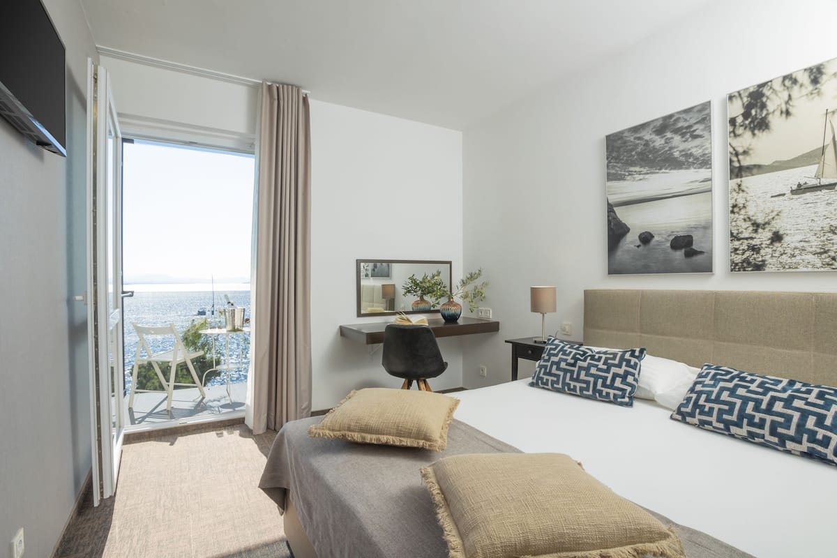 Ein Hotelzimmer mit einem Bett, einem Schreibtisch mit Stuhl, einem Fenster mit Meerblick und einem Bild an der Wand.
