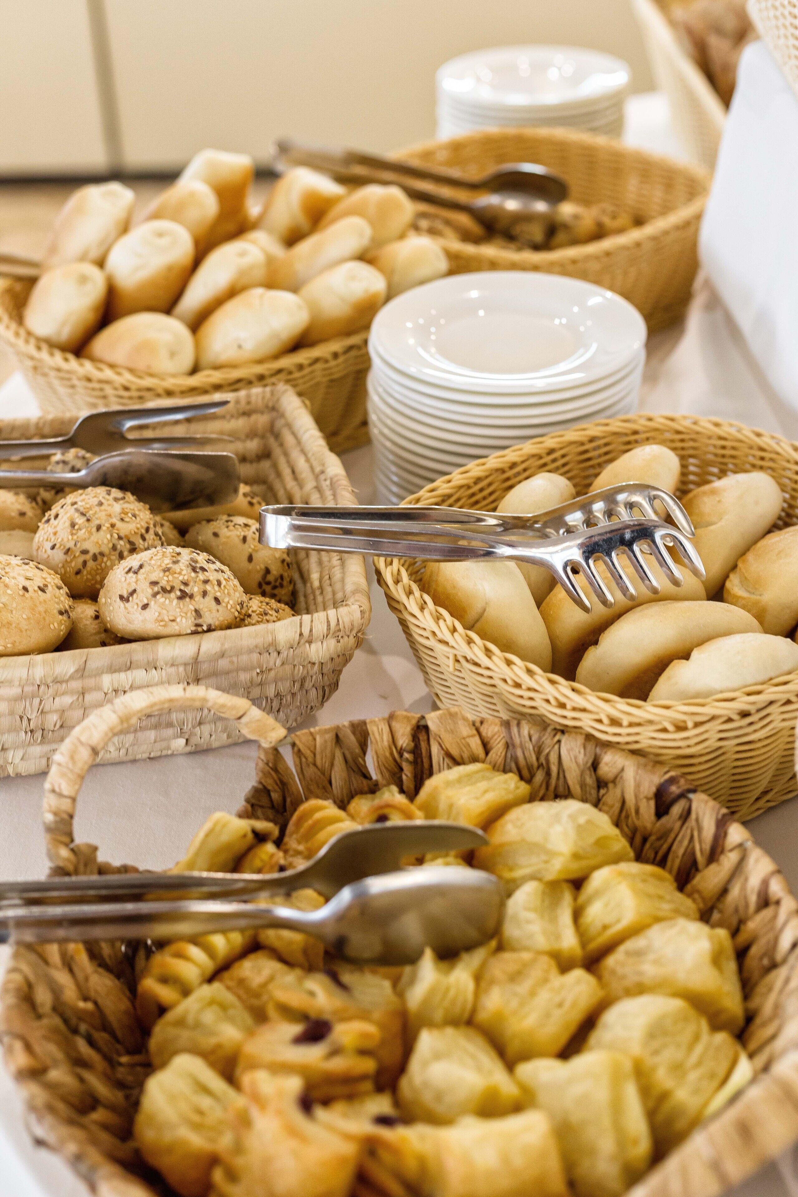 A buffet table with various baked goods in baskets, including bread rolls and pastries.