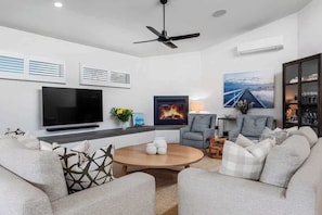 A modern living room with a flat-screen TV, a fireplace, a ceiling fan, and a large window with a view.