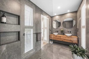 A modern bathroom with a grey tiled wall, a wooden vanity, a large mirror, and a potted plant.