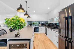 A modern kitchen with white cabinets, a stainless steel refrigerator, and a wooden island with pendant lighting.