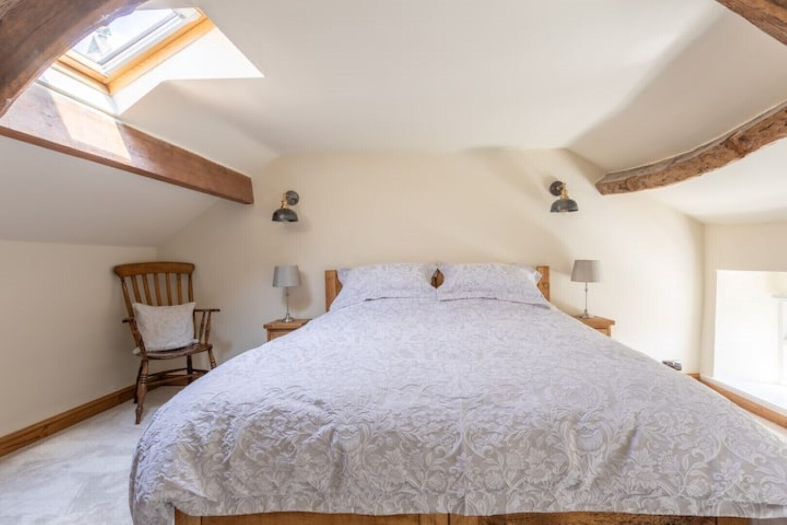 A bedroom with a large bed, a wooden chair, two bedside lamps, and a skylight.