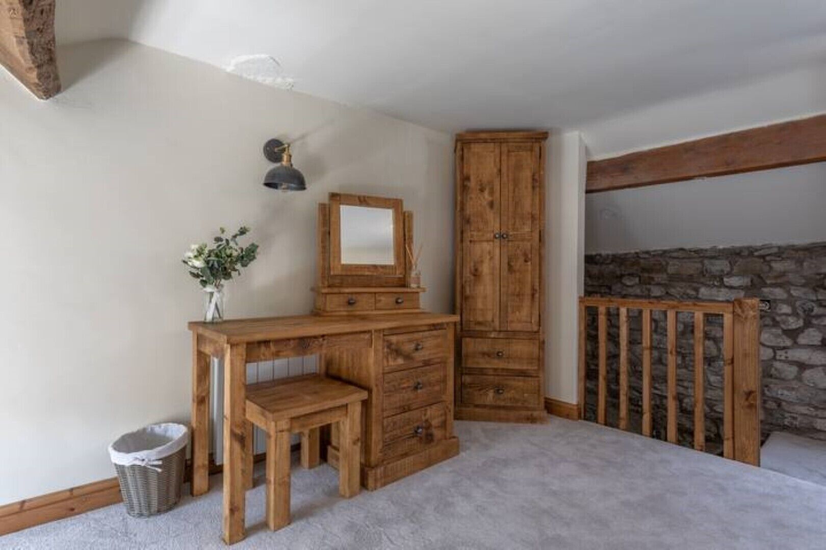 A room with a wooden desk, a mirror, a cabinet, and a stone wall.