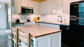 Une cuisine moderne avec des meubles blancs, un réfrigérateur noir, un four à micro-ondes, une cuisinière et un îlot central en bois doté de sièges.