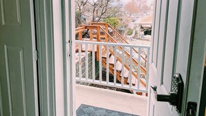 Une porte-fenêtre donnant sur un balcon avec une balustrade en bois et un paillasson en métal.