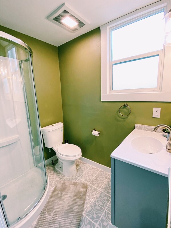 A bathroom with a glass shower enclosure, a toilet, a sink, and a window.