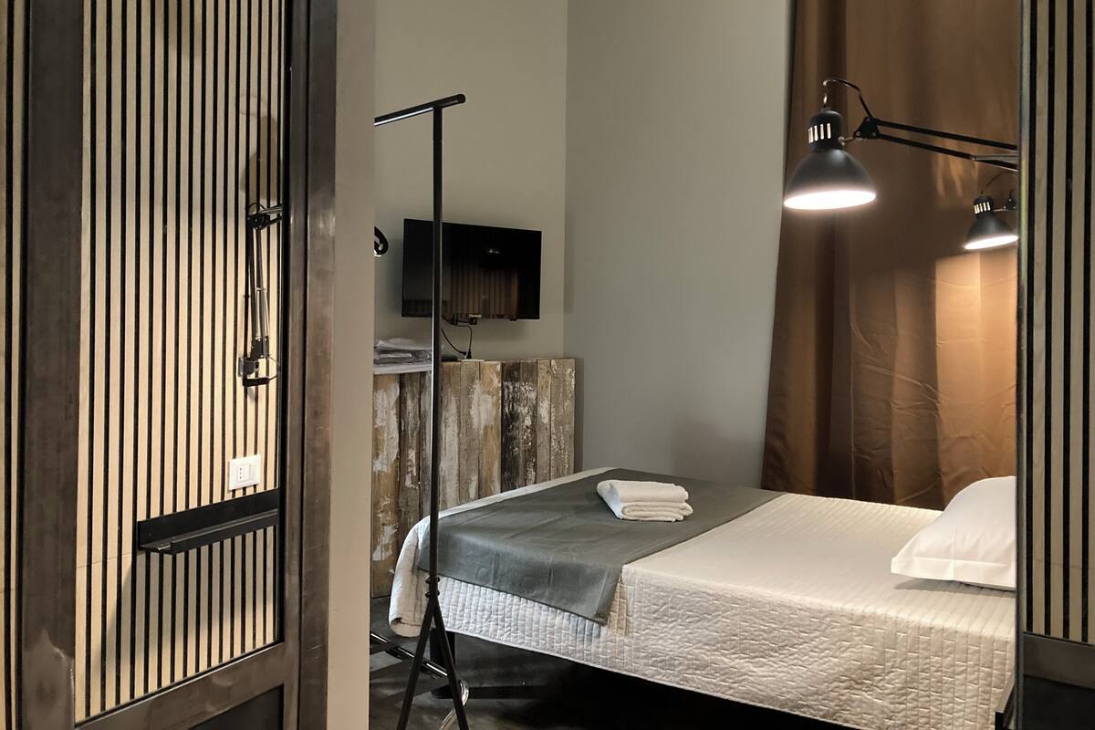 Una habitación de hotel con una cama, un escritorio, un televisor de pantalla plana y una lámpara de pie.