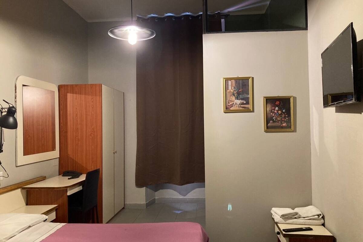 Una habitación de hotel compacta con cama, escritorio, armario y televisión en la pared.