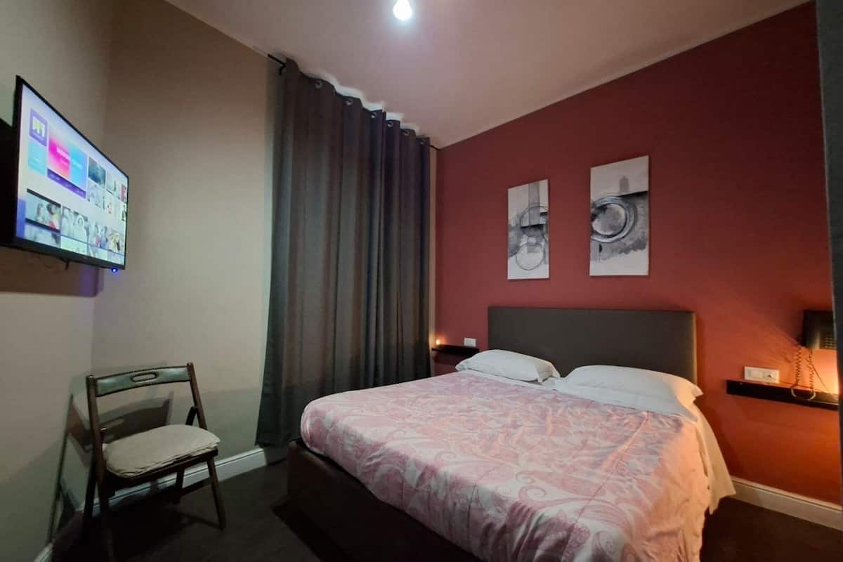 Habitación de hotel con una cama, una silla, un televisor montado en la pared y dos obras de arte decorando la pared.