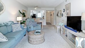 A living room with a sofa, armchair, and ottoman, a television, and a bookshelf.