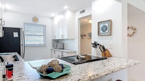 A modern kitchen with white cabinets, a granite countertop, a built-in microwave, and a stainless steel refrigerator.