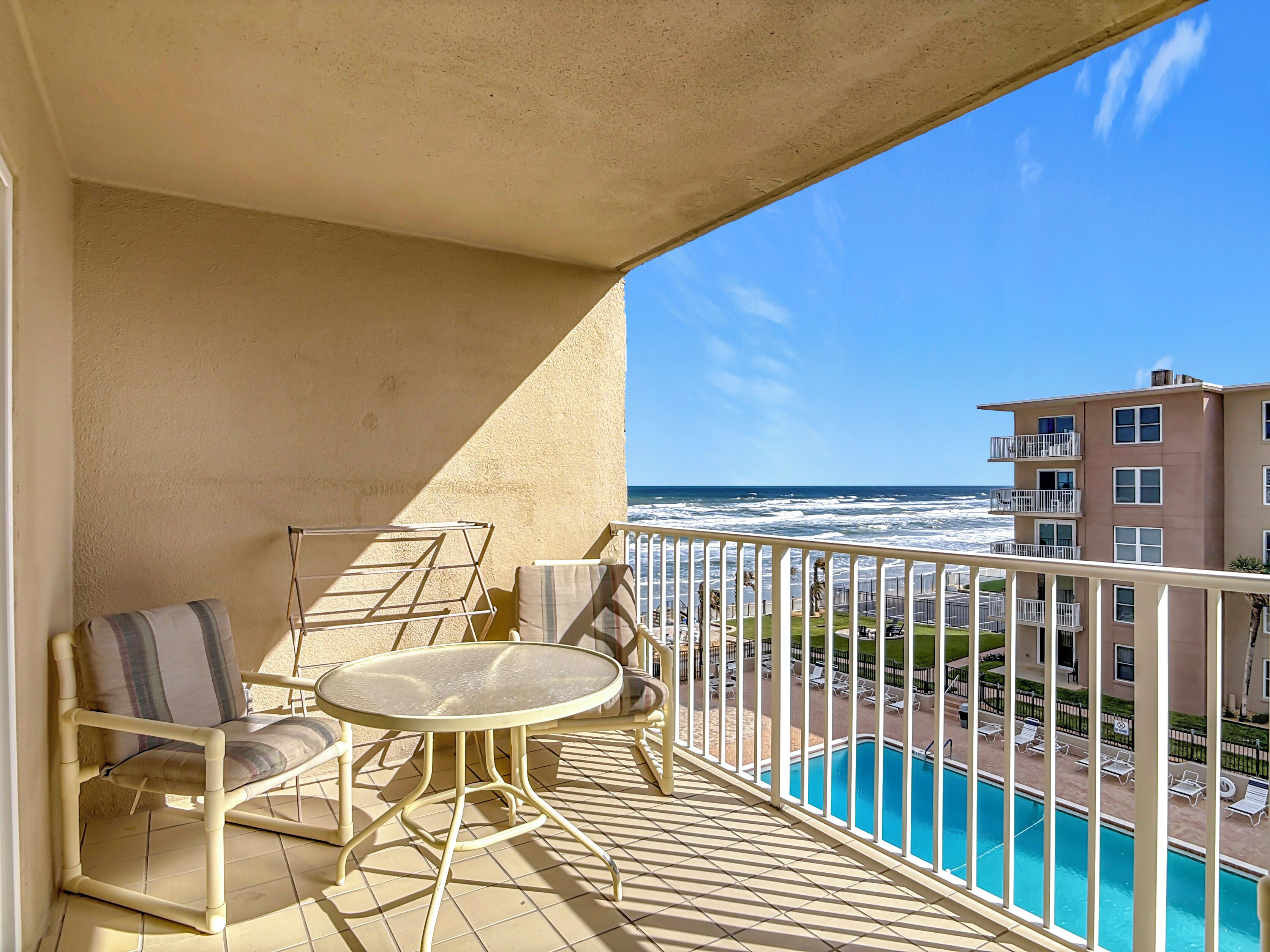 A balcony with a table and chairs, overlooking a swimming pool and ocean view.