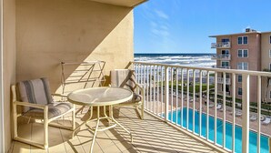 A balcony with a table and chairs, overlooking a swimming pool and ocean view. - Direct Oceanfront Complex on the No Drive Beach in NSB! (New Smyrna Beach)