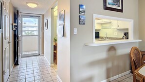 A hallway with a tiled floor, a door, and a view into a kitchen area with a countertop and cabinets. - Direct Oceanfront Complex on the No Drive Beach in NSB! (New Smyrna Beach)