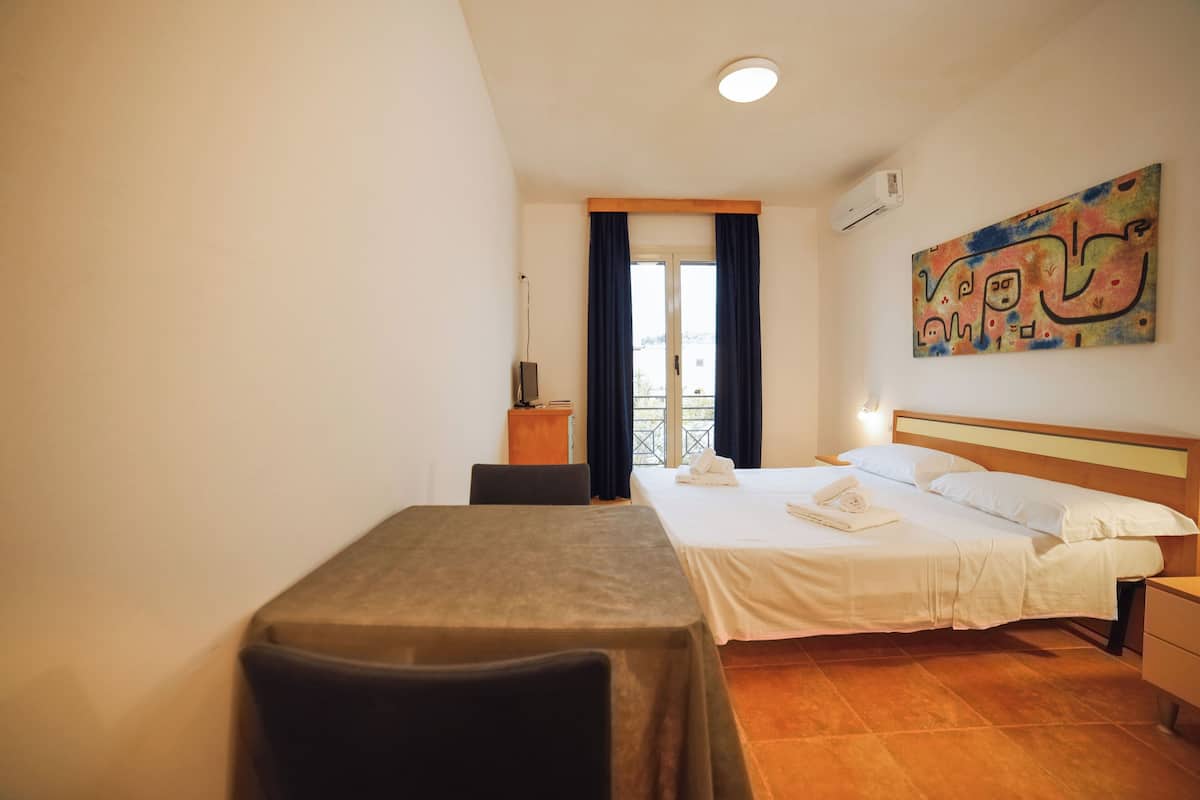 Una habitación de hotel con una cama, un escritorio, una silla, una mesita y un cuadro en la pared.
