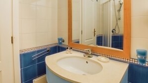 Un baño con lavamanos, espejo y paredes con azulejos azules.