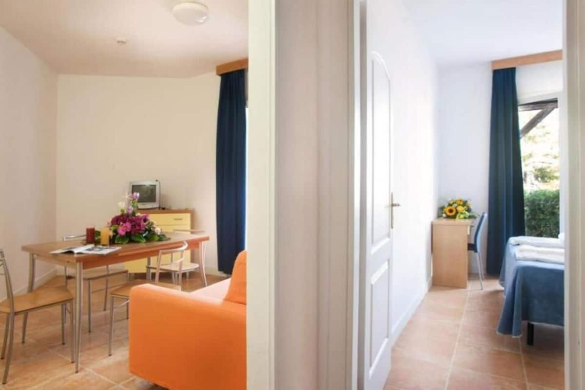 Habitación de hotel compacta con zona de comedor, una pequeña kitchenette y una cama.