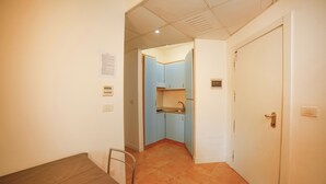 Un pasillo estrecho con una mesa y sillas para comer, que conduce a una cocina con armarios azules y una puerta blanca.