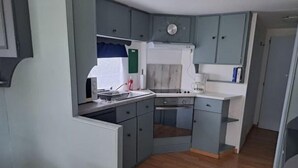 Une cuisine compacte avec des meubles gris, un plan de travail blanc et un four encastré.